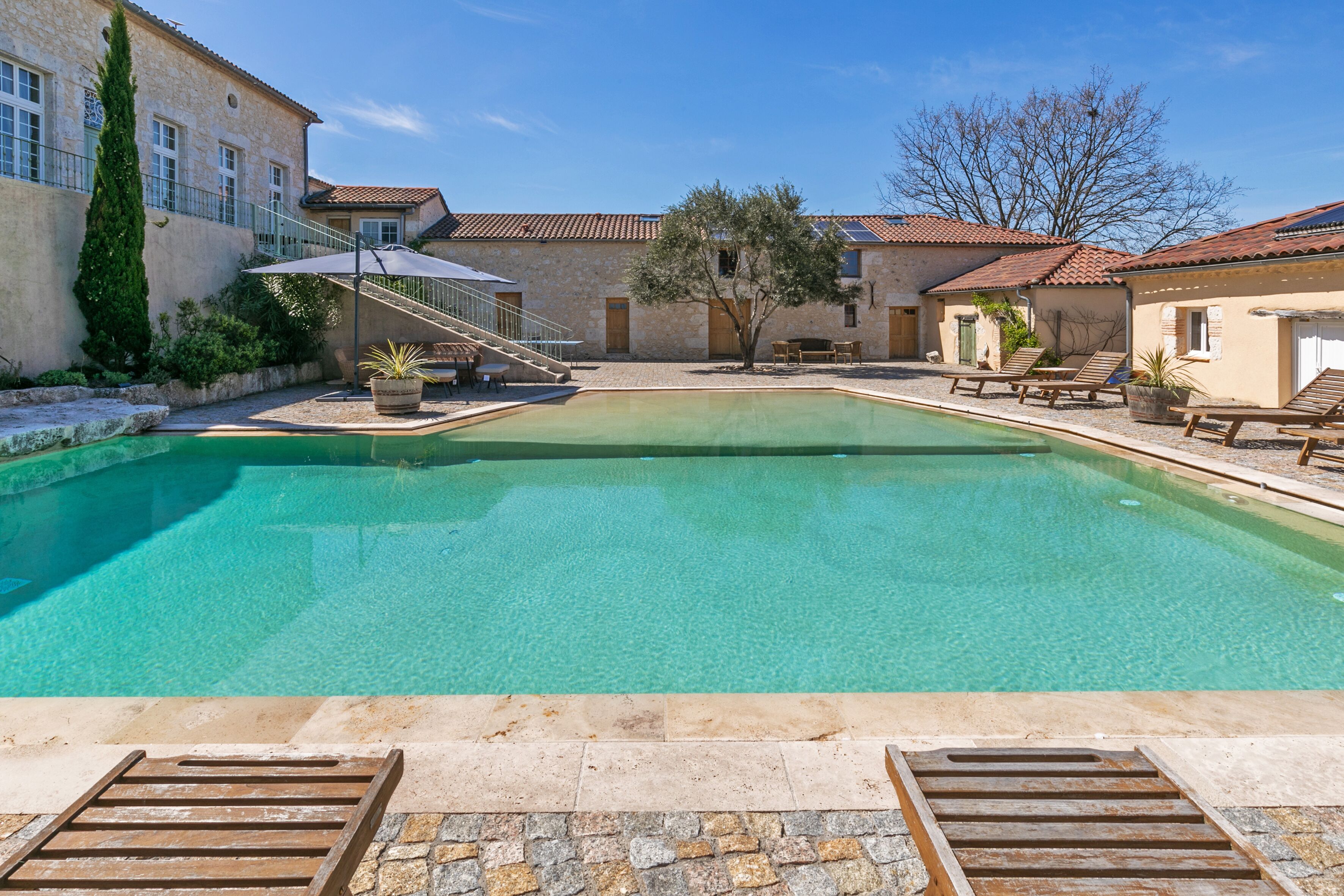 A swimming pool with a stone deck and lounge chairs.