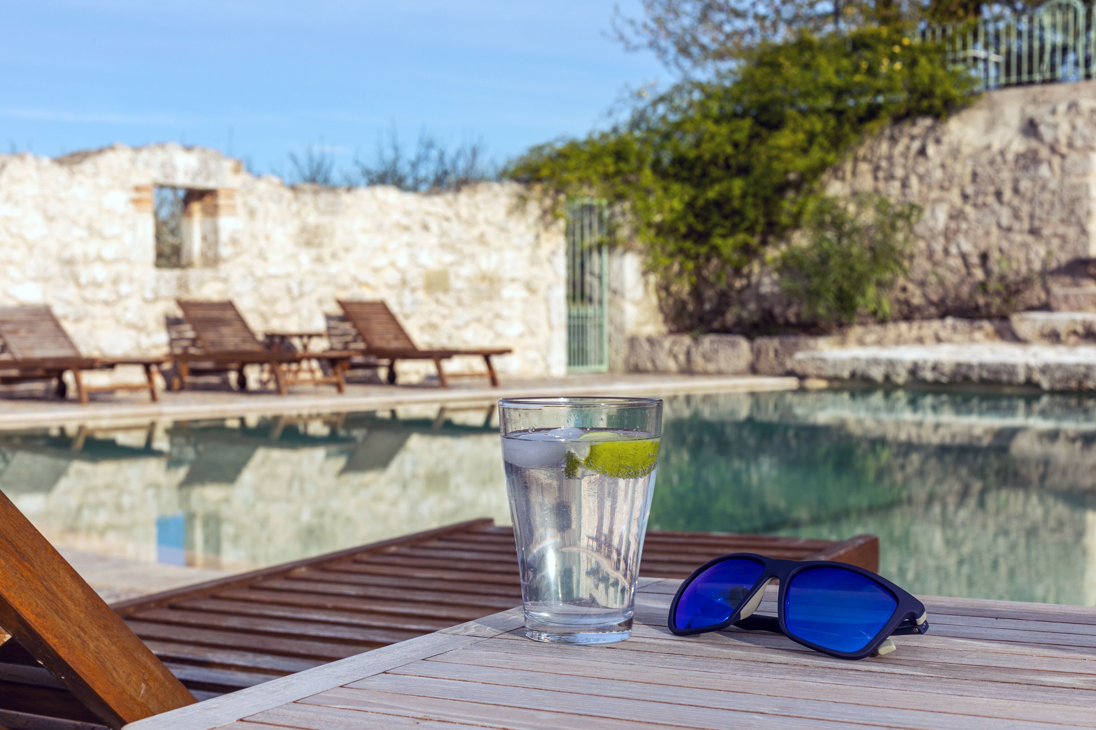 A clear glass of water with a lime slice on a wooden table by a poolside.