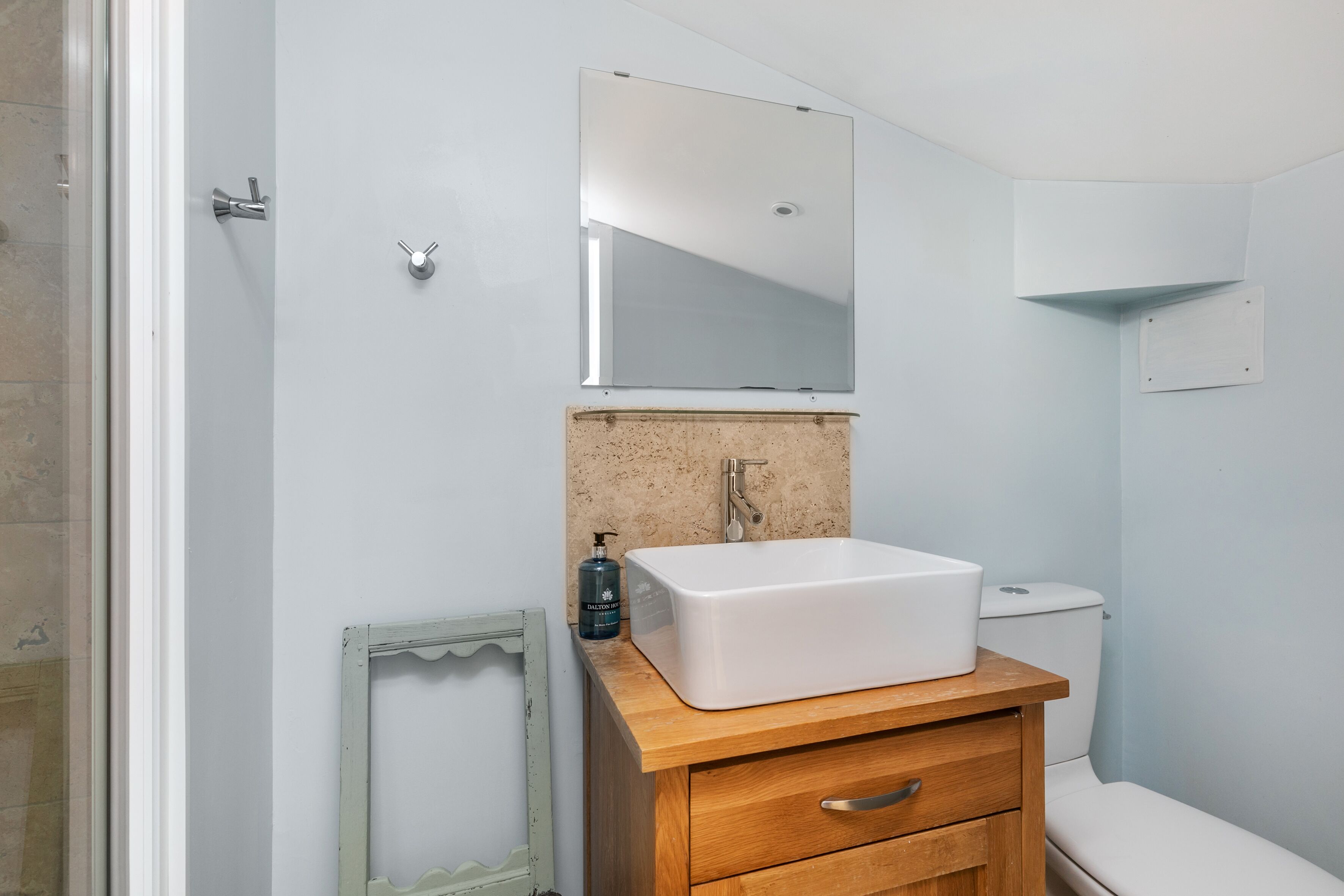 A bathroom with a white sink, wooden vanity, a mirror, and a toilet.
