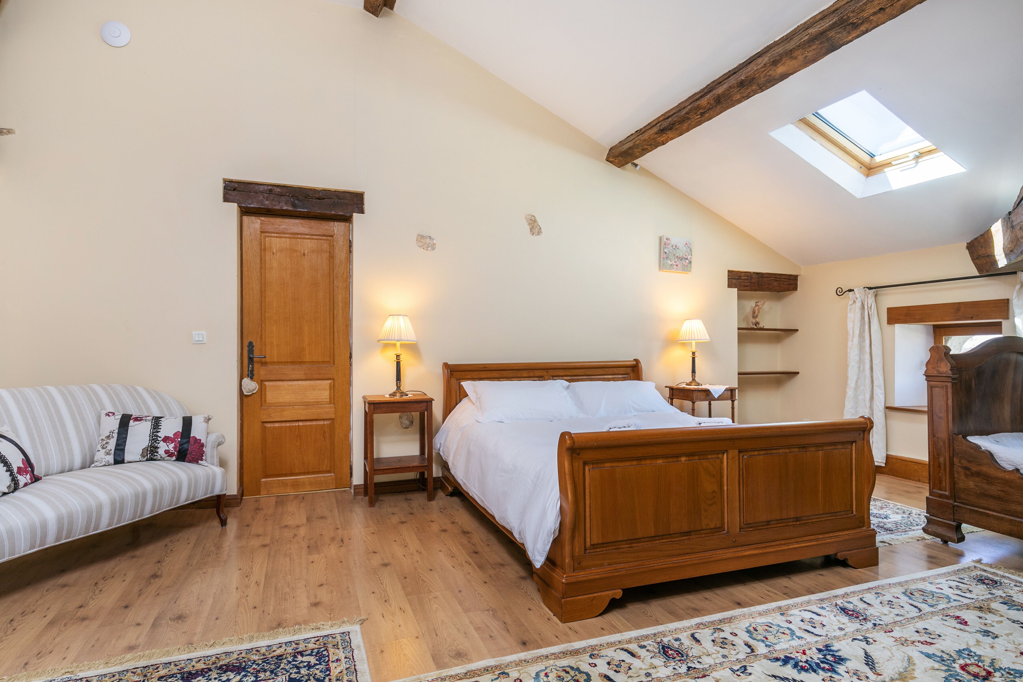 A bedroom with a wooden bed, a sofa, a skylight, and a wooden ceiling.