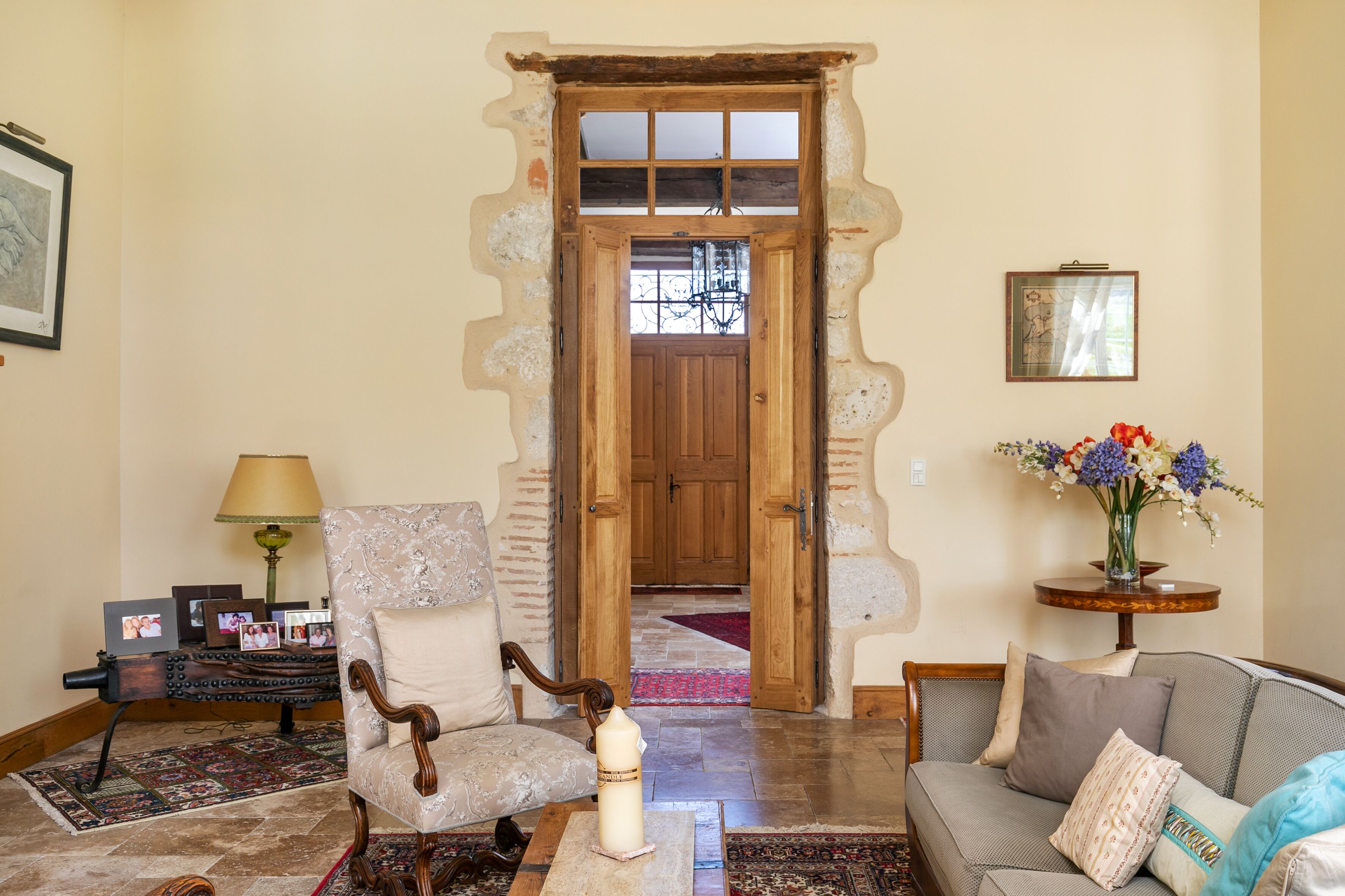 A living room with a wooden door, a sofa, a chair, a lamp, and a vase with flowers.