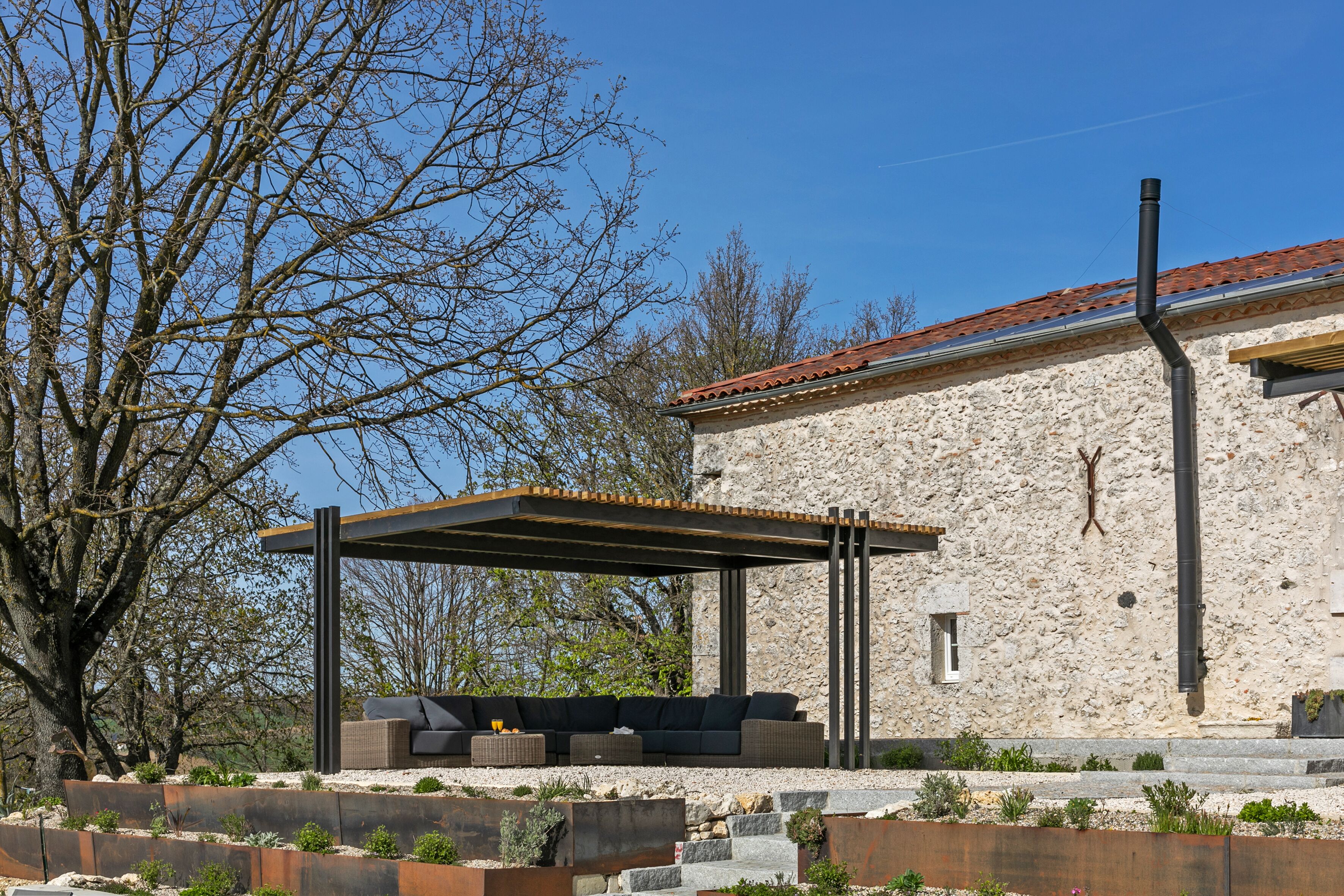 A stone building with a covered outdoor seating area and a large tree in the background.