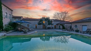 A swimming pool with a sunset view, surrounded by buildings with tiled roofs and outdoor seating. - Domaine de Rambeau (Castelmoron-sur-Lot)
