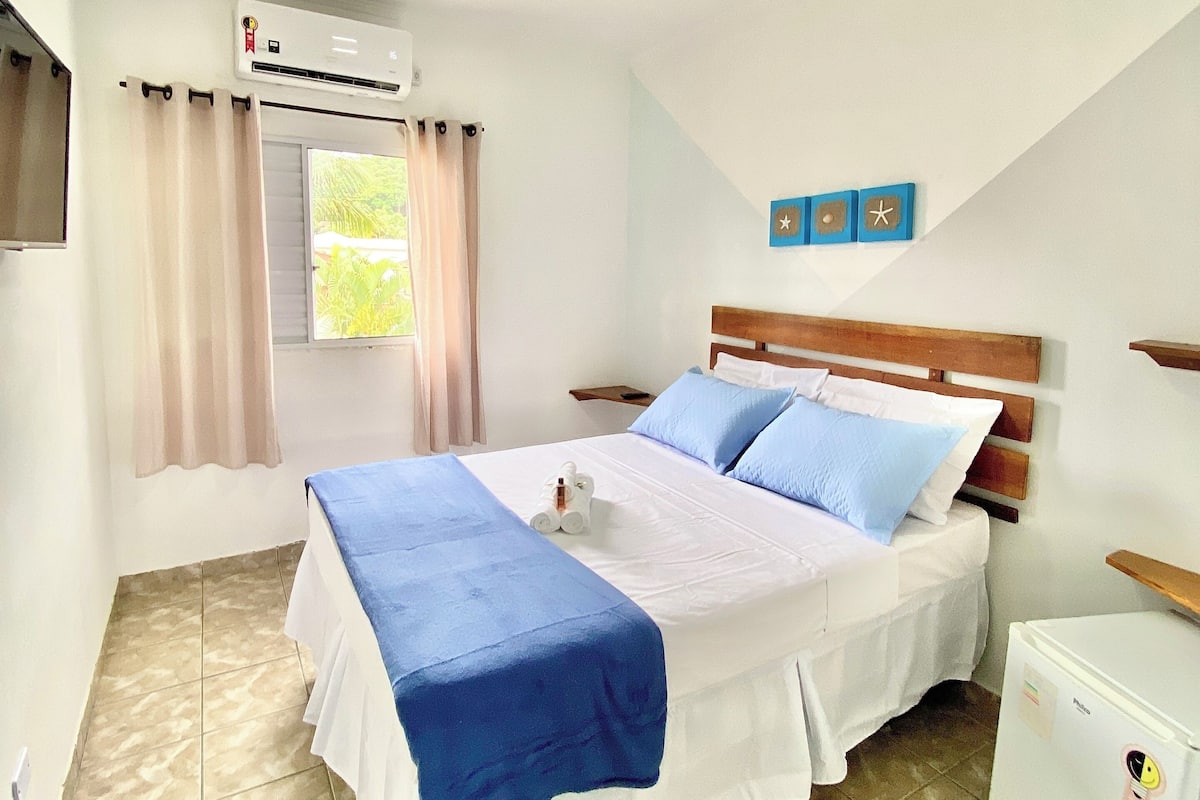 A bedroom with a bed, a small white refrigerator, and a window with curtains.