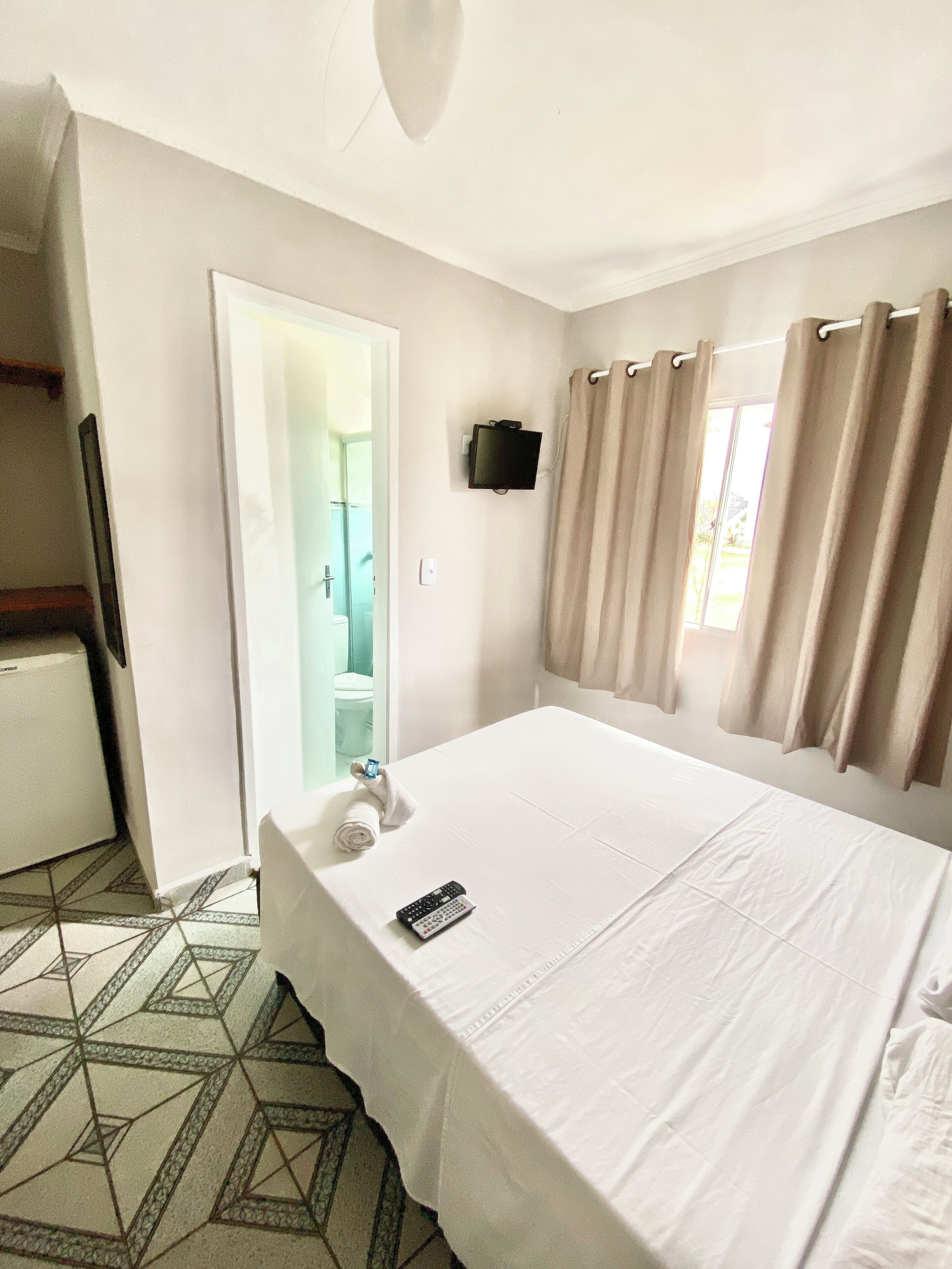 A hotel room with a bed, a TV mounted on the wall, a bathroom visible through an open door, and a patterned floor.