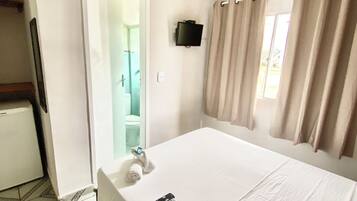 A hotel room with a bed, a TV mounted on the wall, a bathroom visible through an open door, and a patterned floor.