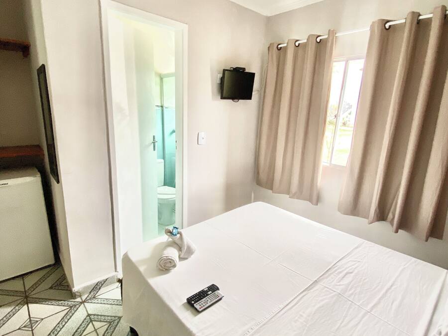 A hotel room with a bed, a TV mounted on the wall, a bathroom visible through an open door, and a patterned floor.