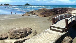 A beach with rocky formations, a wooden walkway, and the ocean in the background. - Pousada Dolce Vita (Itanhaém)
