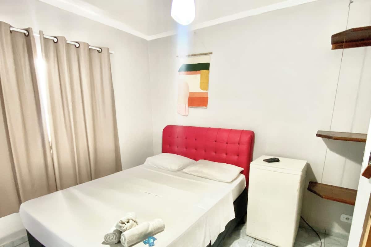 A hotel room with a bed, a small bedside table, a ceiling fan, and a window with curtains.