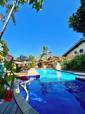Una piscina con agua cristalina, rodeada de exuberante vegetación y un cielo azul despejado.