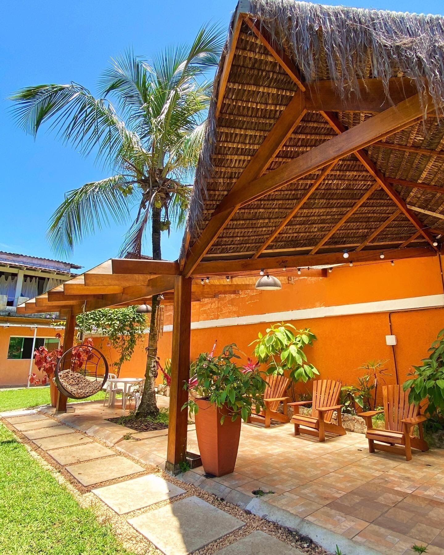 A covered outdoor area with a thatched roof, wooden chairs, and potted plants.