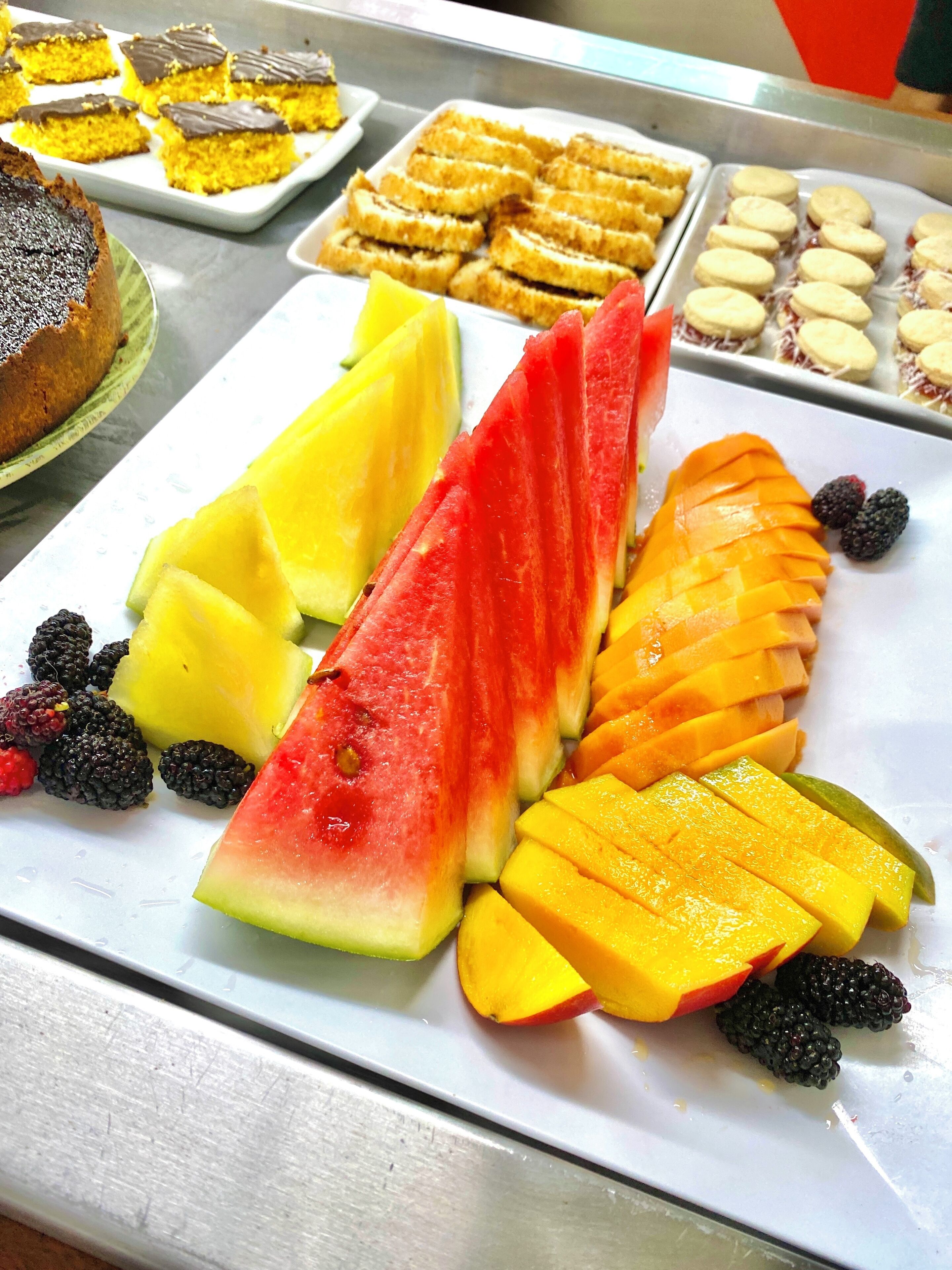 A buffet with various food items including sliced watermelon, mango, pineapple, and blackberries.