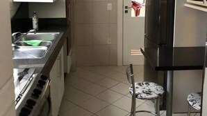 A compact kitchen with a stove, sink, and a refrigerator. There is a small table with two chairs. - Apto Perfeito Quadra Mar (Balneário Camboriú)