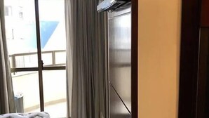 A hotel room with a bed, a flat-screen TV, a sliding glass door leading to a balcony, and a tiled floor. - Apto Perfeito Quadra Mar (Balneário Camboriú)