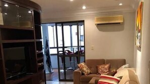 A living room with a sofa, TV stand, and a sliding glass door leading to a balcony. - Apto Perfeito Quadra Mar (Balneário Camboriú)