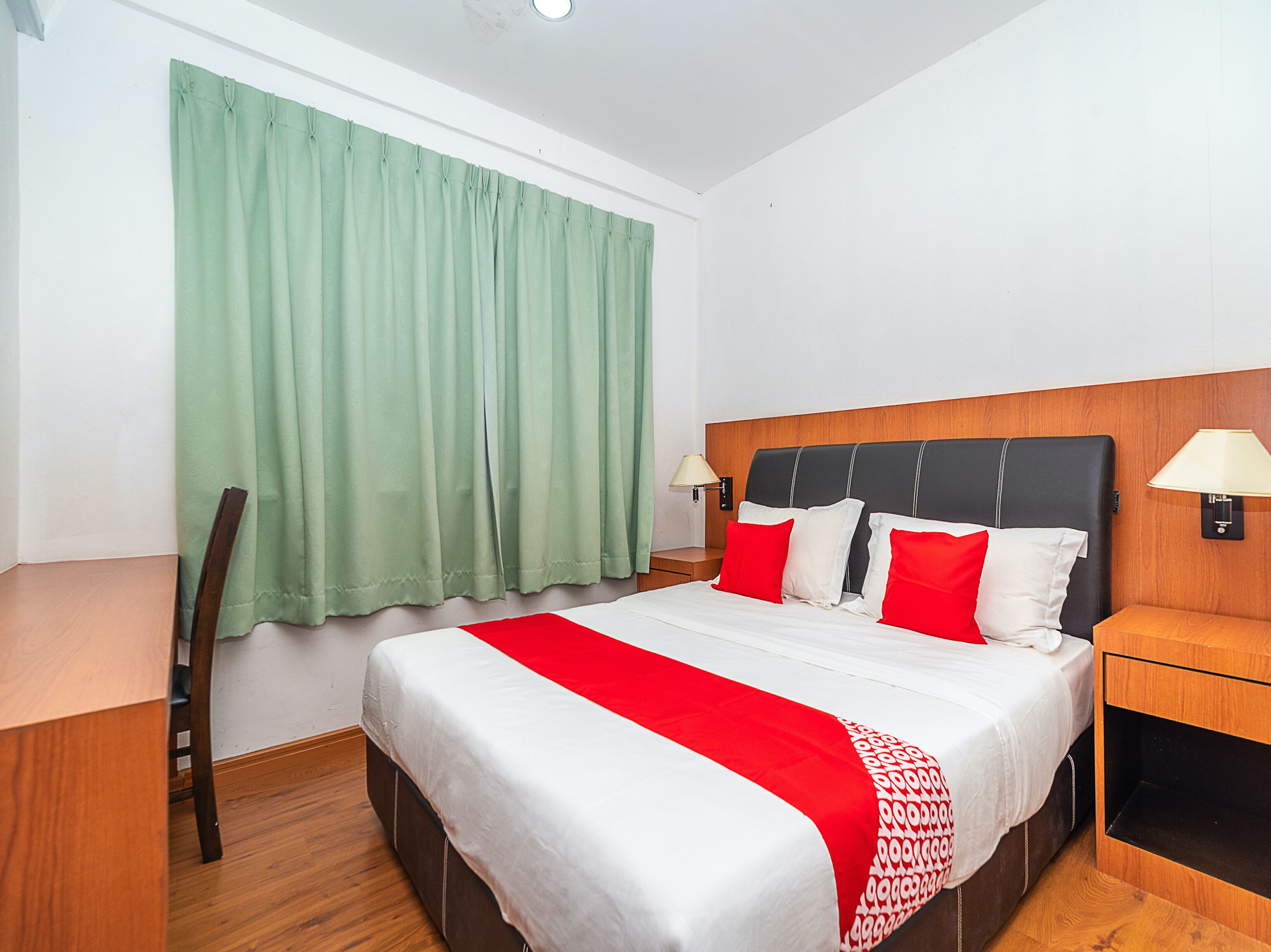 A hotel room with a bed, two bedside tables, a chair, a desk, and a window with curtains.