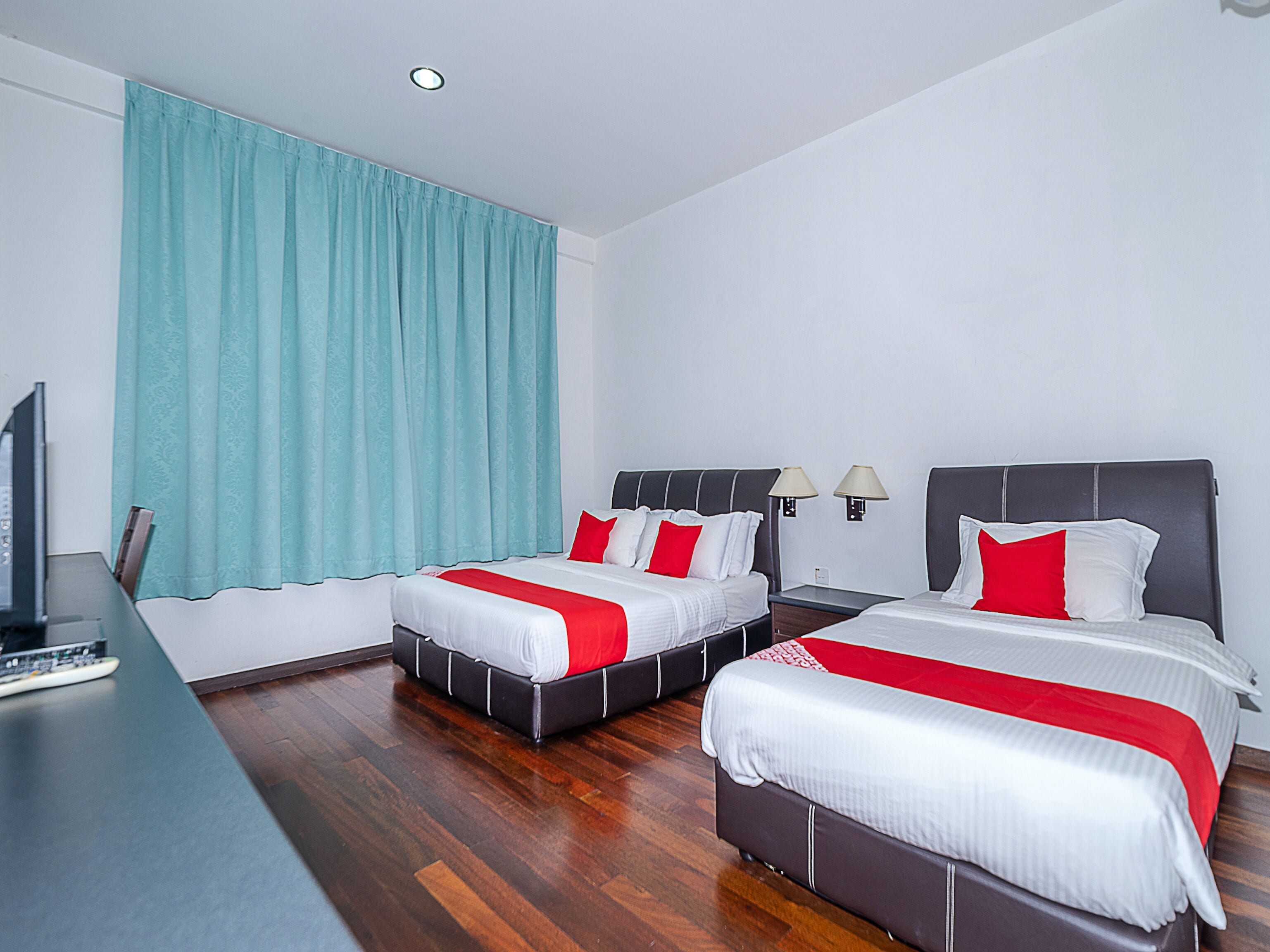 A hotel room with two beds, a desk with a computer, and a window with curtains.