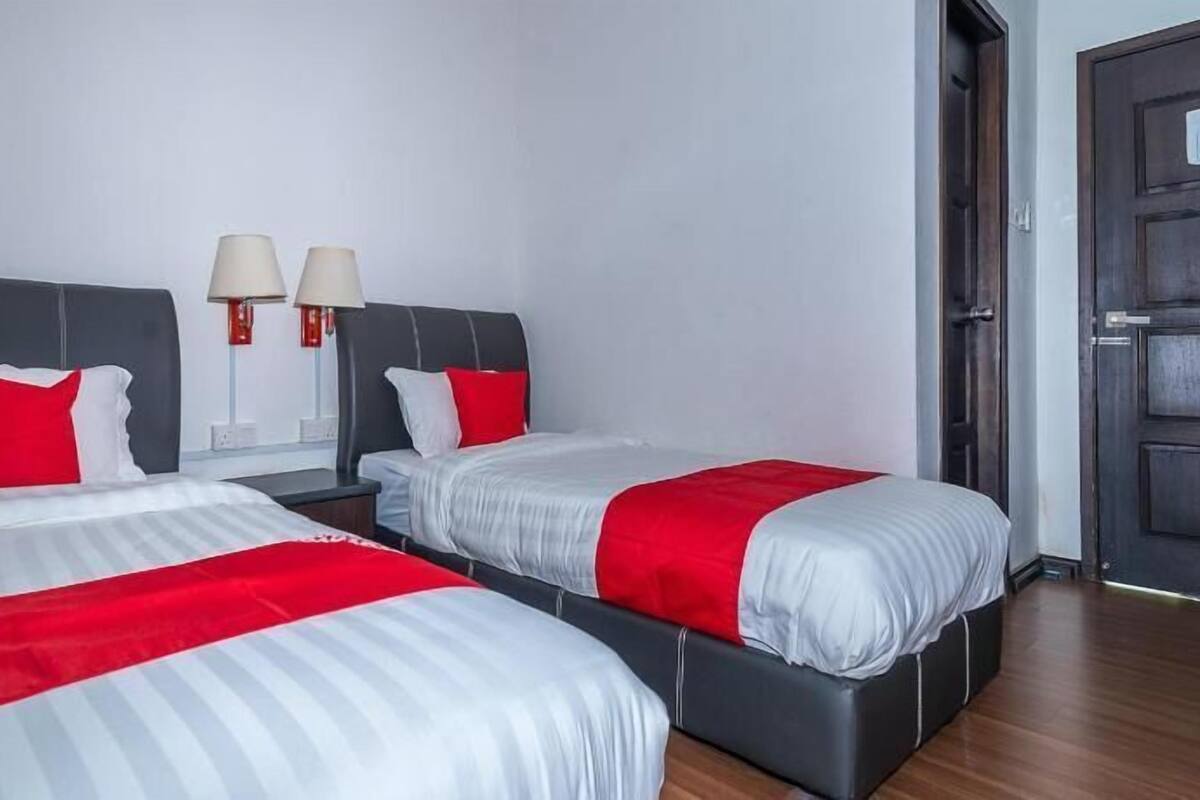Habitación de hotel con dos camas, cada una con una colcha rojo y blanco, un cabecero oscuro y dos lámparas de noche.