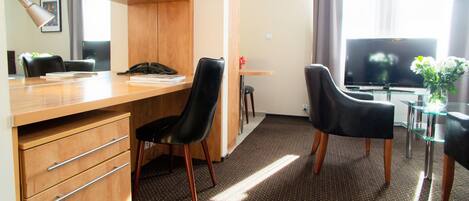 A hotel room with a wooden desk, two black chairs, a television, and a small table with a plant.