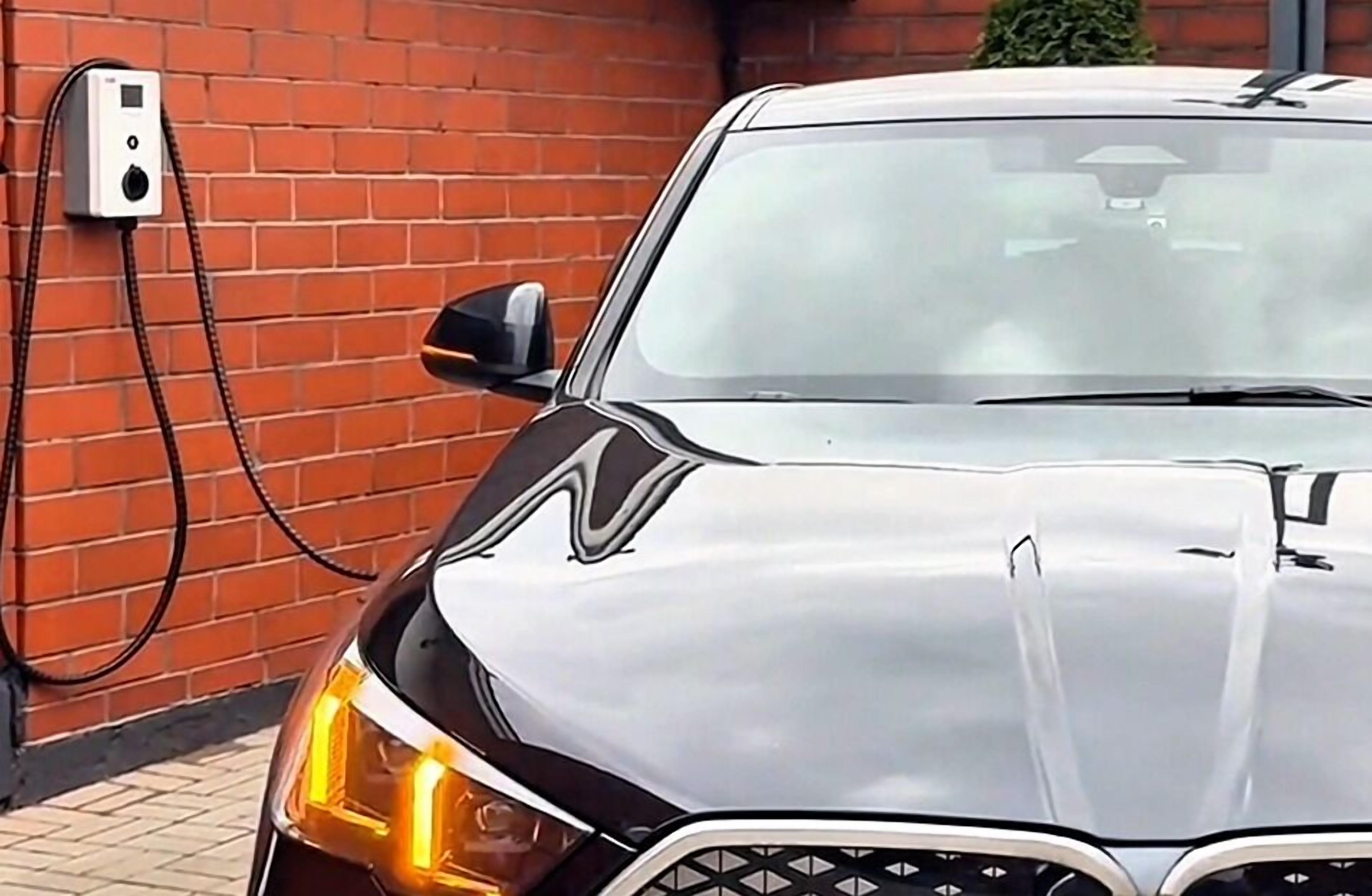 Een auto geparkeerd voor een bakstenen muur met een laadstation.