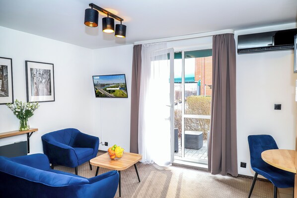 A modern room with a sofa, chairs, a small table with fruit, a TV, and a view through the window. - Warsaw - Apartments Apartamenty Sadyba (Warsaw)