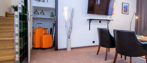 A hotel room with a TV, a desk, two chairs, a suitcase, and a coat rack.