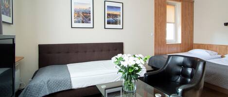 Habitación de hotel con una cama, una silla, un escritorio con un florero y dos cuadros en la pared.