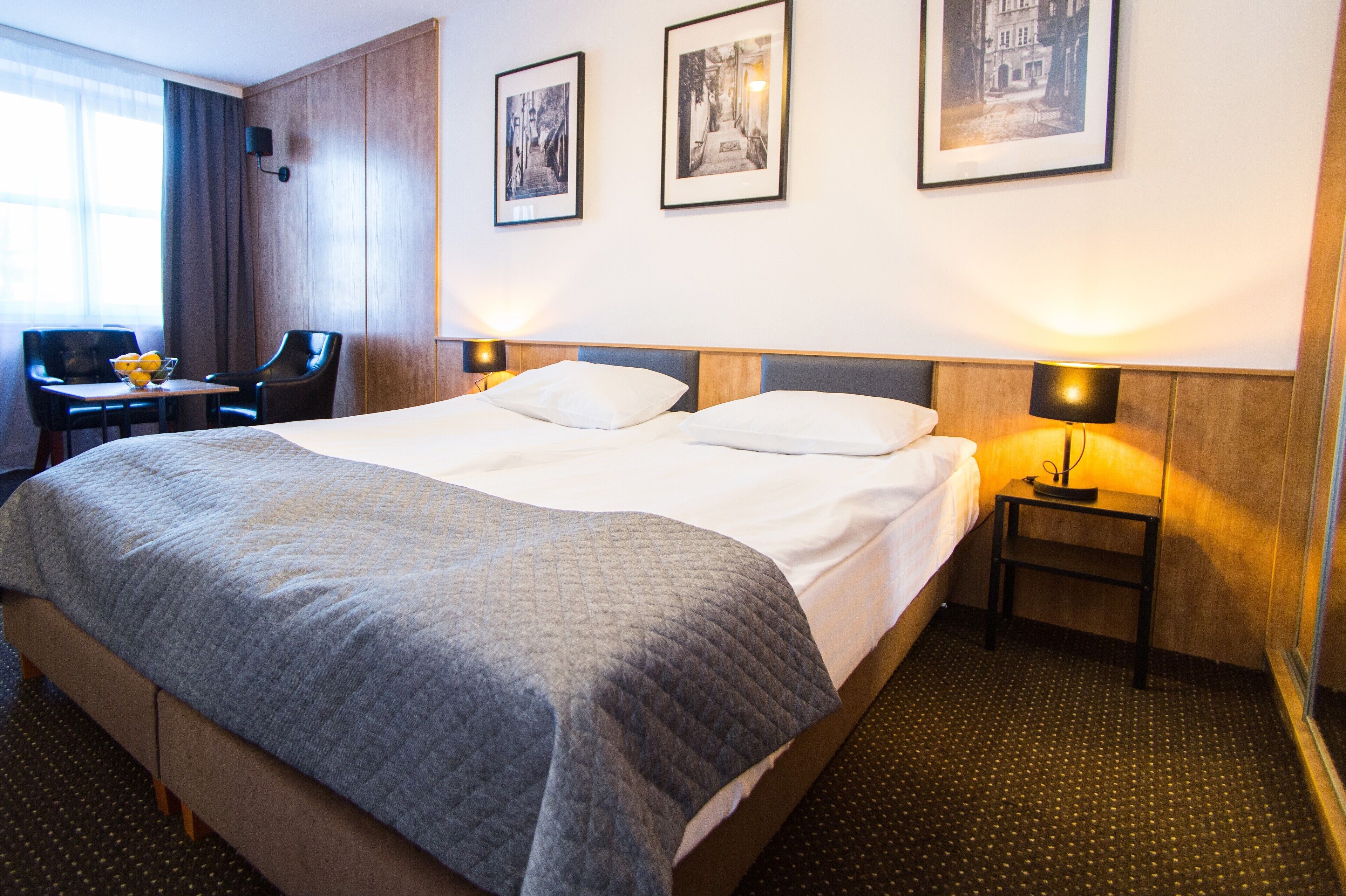 A hotel room with a large bed, two bedside lamps, a desk with a chair, and three framed pictures on the wall.