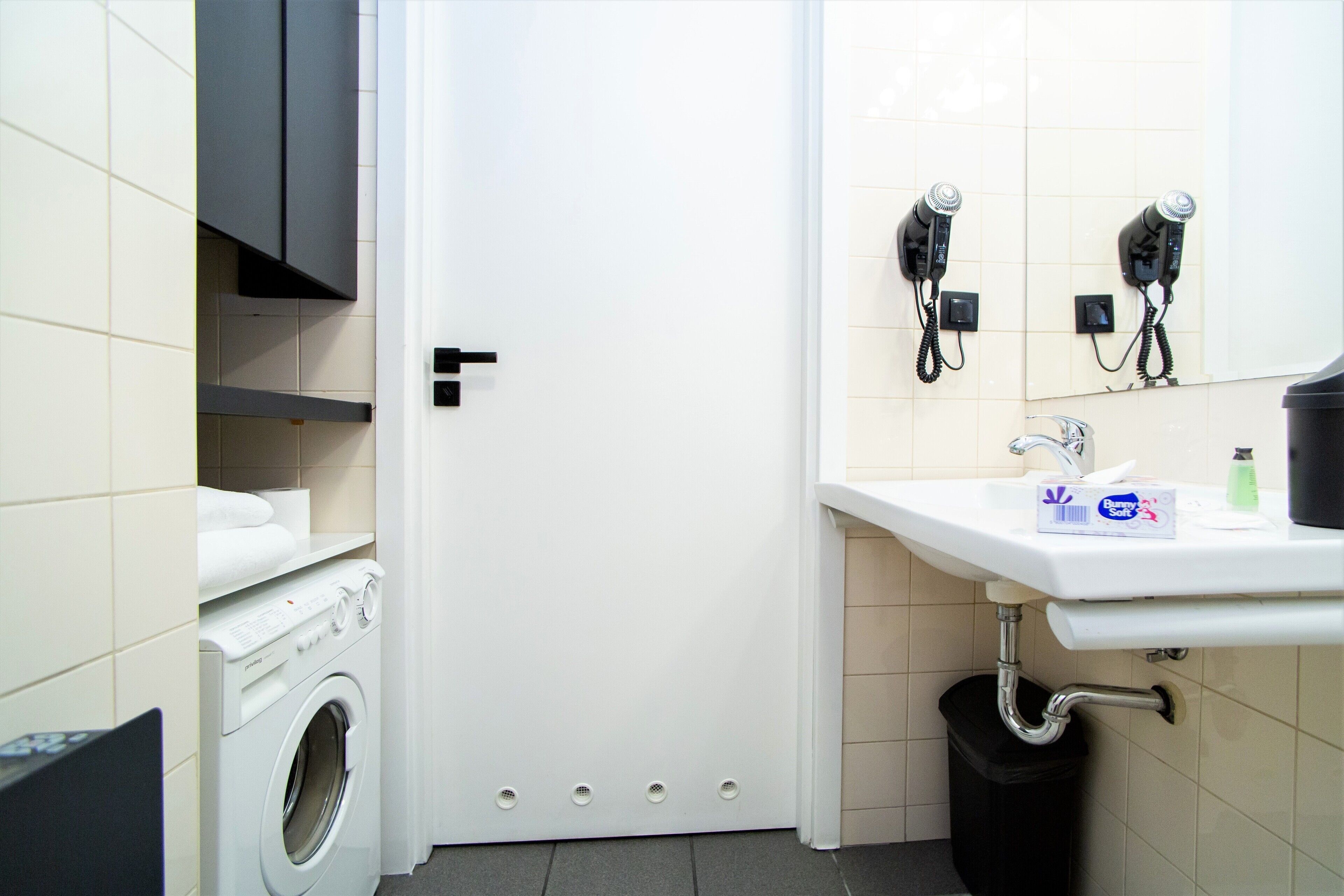 A modern bathroom with a washing machine, a sink with a mirror, and two hair dryers mounted on the wall.