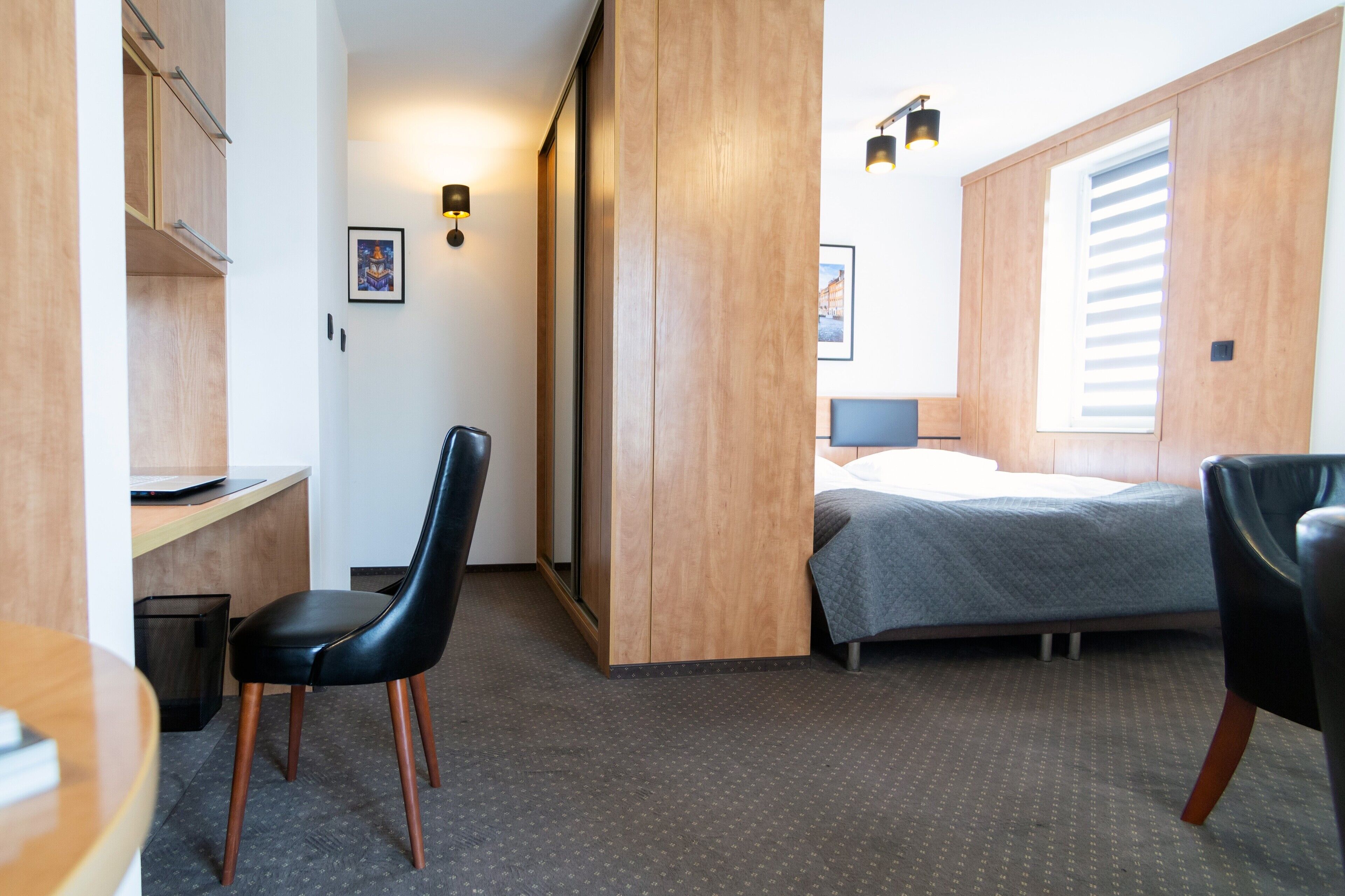 A compact hotel room with a bed, a desk, a chair, and a wardrobe.