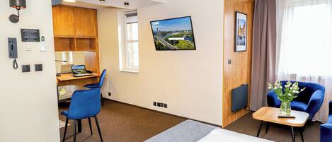 A hotel room with a bed, a desk, a chair, a TV, and a window with curtains.