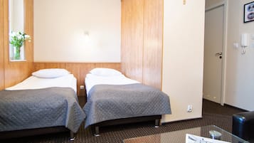 A hotel room with two beds, a glass table, and a small window with flowers.