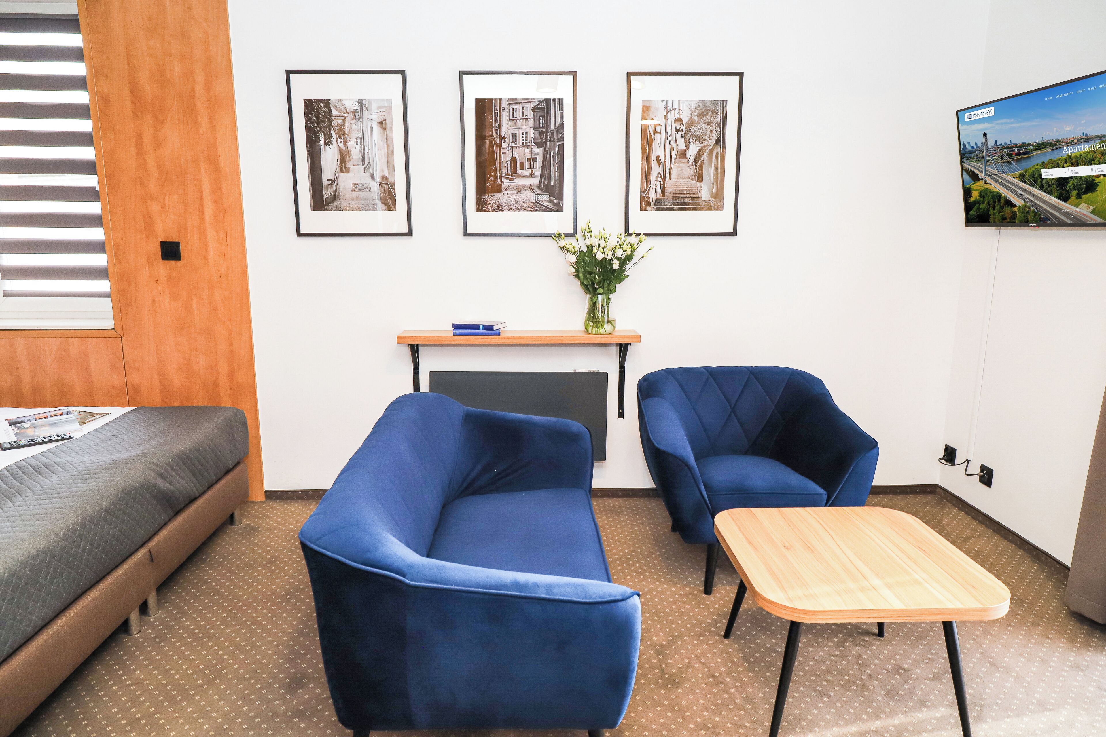 A hotel room with a bed, a blue sofa, a small table, and three framed pictures on the wall.