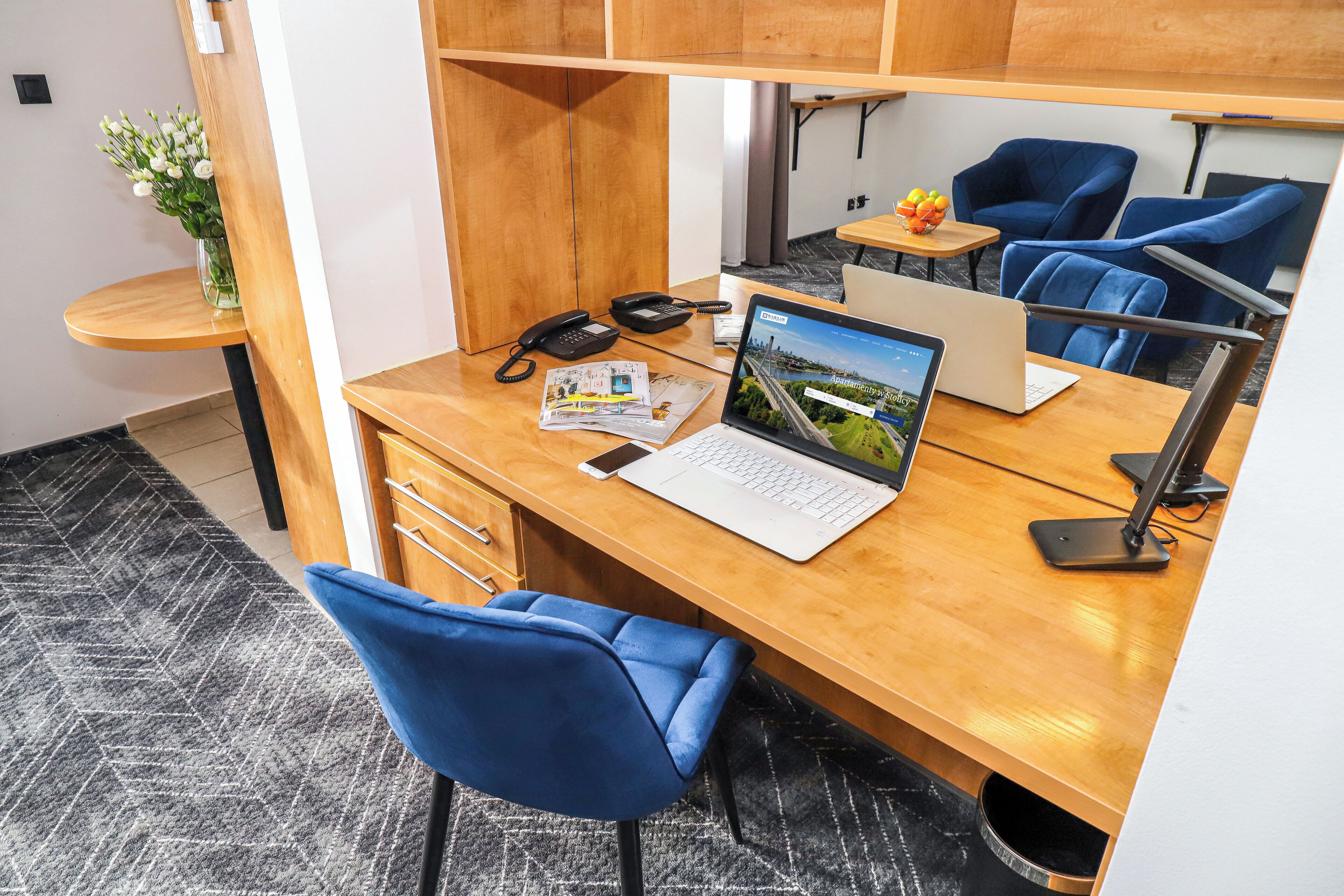 Un espacio de oficina moderno con un escritorio de madera, una computadora portátil, un teléfono y una silla azul.