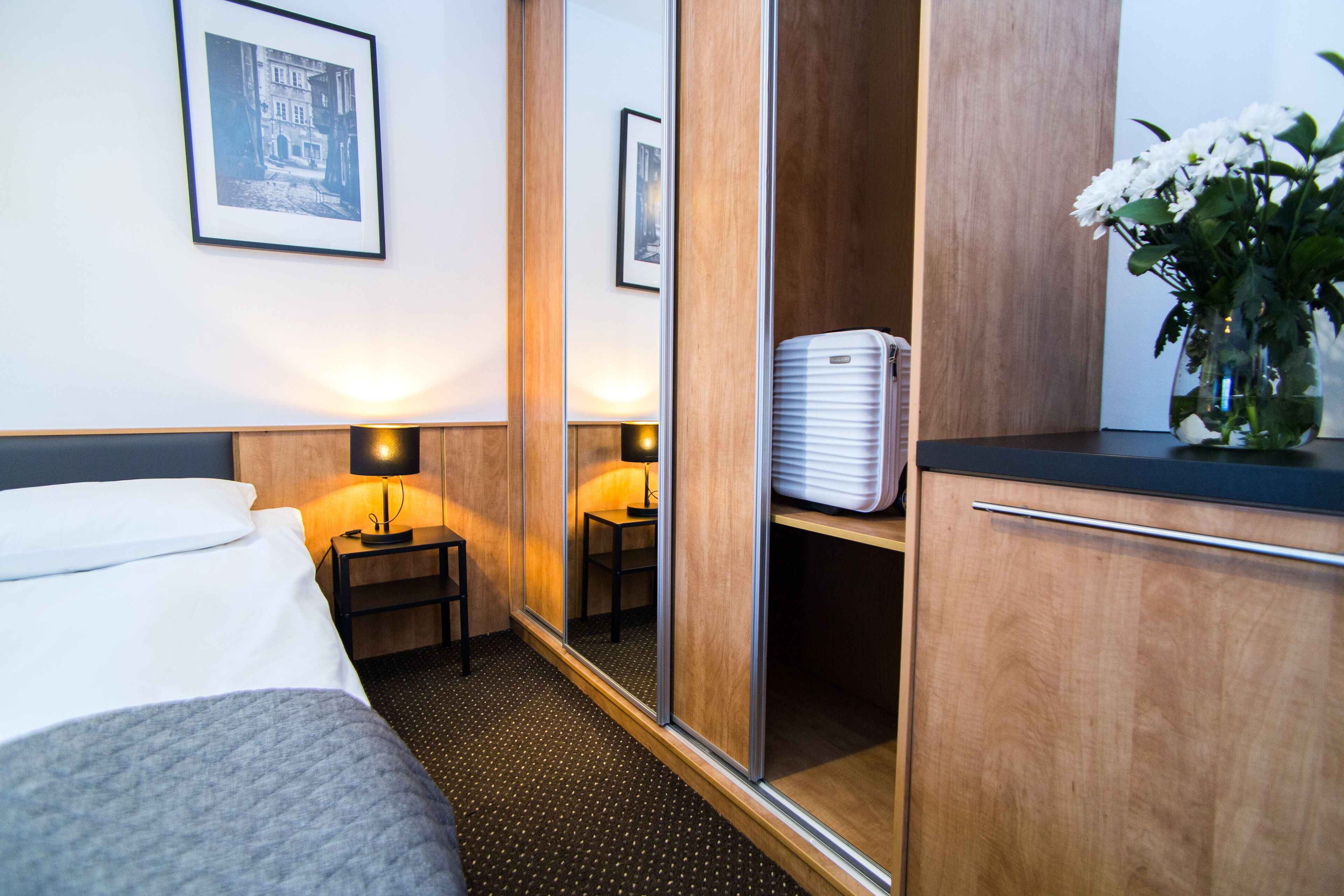 A hotel room with a bed, bedside lamps, a wardrobe, a mirror, and a small table with a lamp.