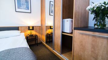A hotel room with a bed, bedside lamps, a wardrobe, a mirror, and a small table with a lamp.