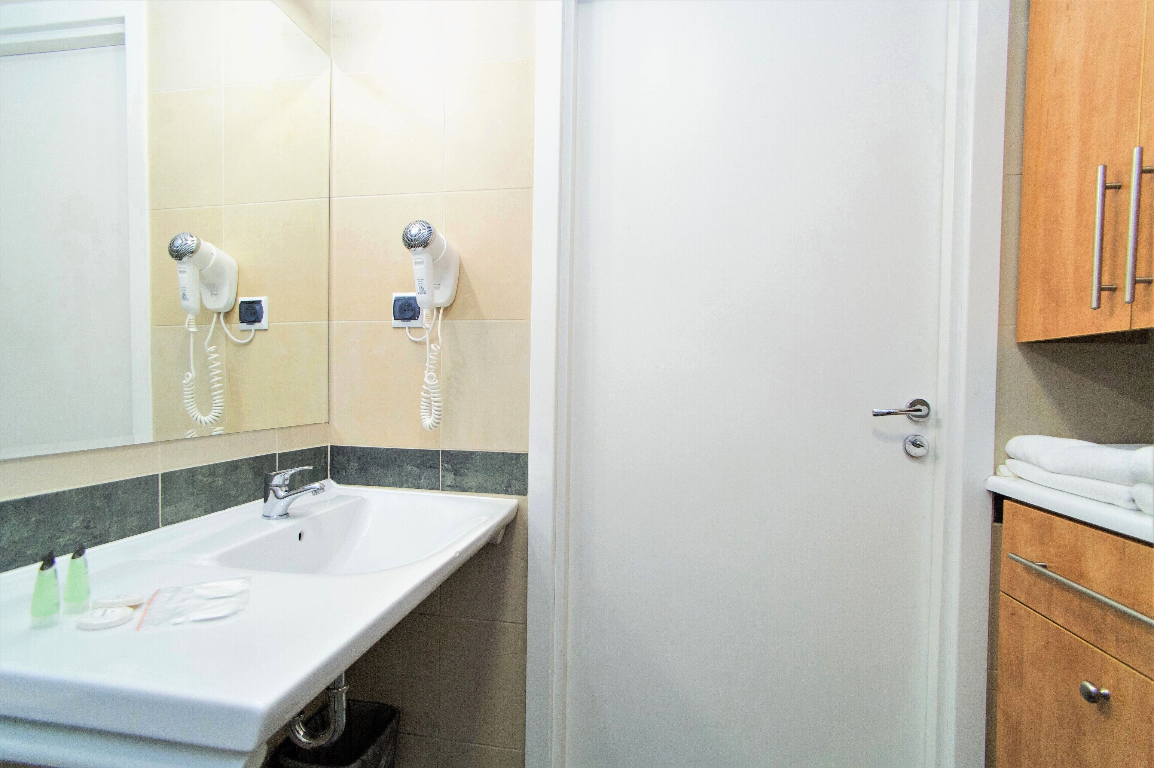 Un baño con un lavamanos blanco, espejo y dos secadores de pelo montados en la pared.