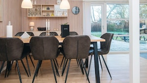 A modern dining area with a wooden table, dark upholstered chairs, pendant lights, and a view of the outdoors through a glass door. - Cozy Family Cottage - By Traum Ferienwohnungen (Hemmet)