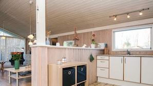 A modern kitchen with wooden cabinets, a countertop, and a window. There is a dining area with a table and chairs, and a vase with flowers. - Cozy Family Cottage - By Traum Ferienwohnungen (Hemmet)