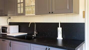A kitchen with grey cabinets, a black countertop, a white microwave, a sink with a faucet, and a roll of paper towels.