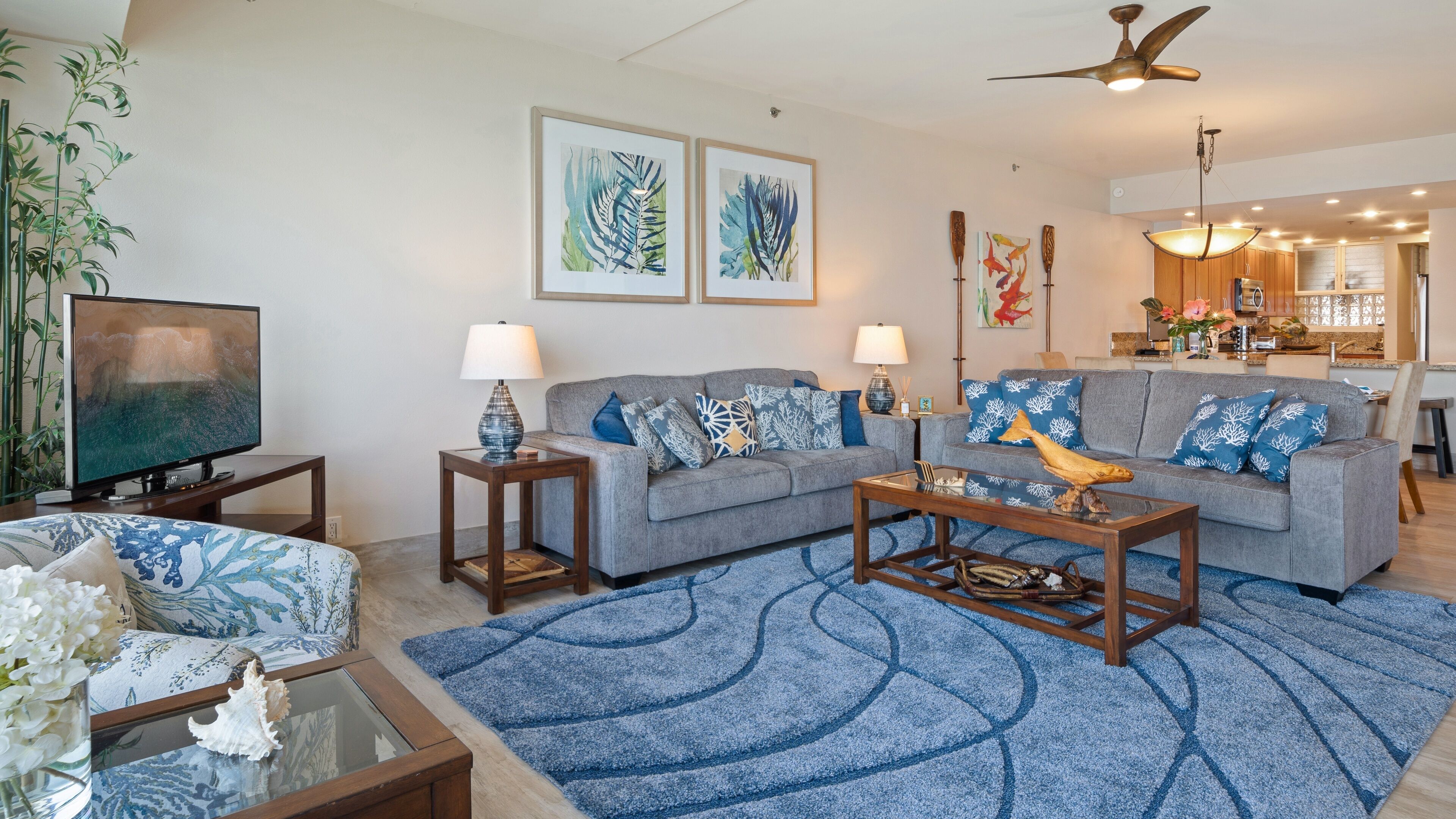 A living room with a sofa, coffee table, and TV. There are two lamps, a rug, and a plant.