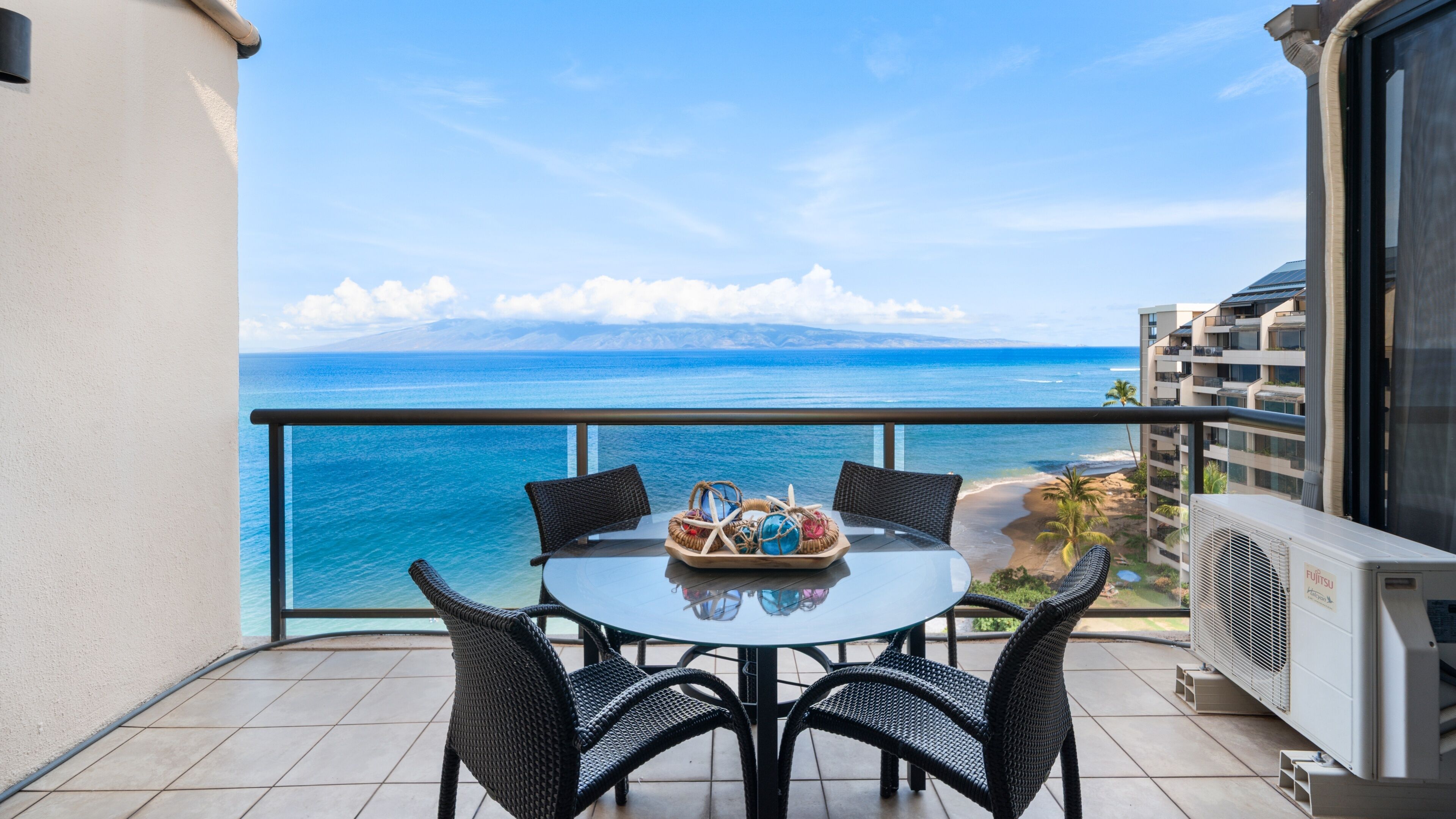 A balcony with a table and chairs, overlooking a beach and ocean.