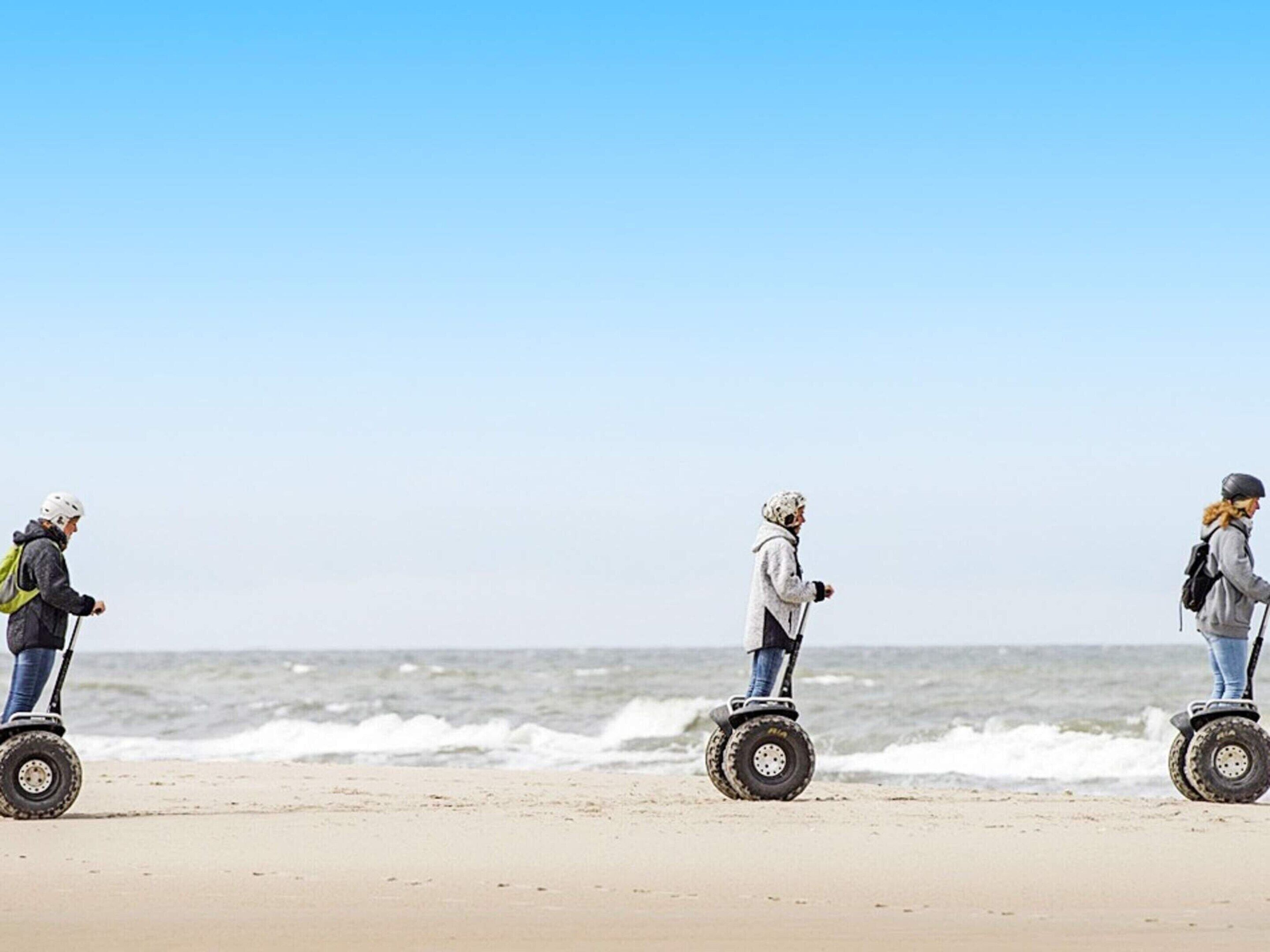 Três pessoas em segways numa praia, com o oceano ao fundo.