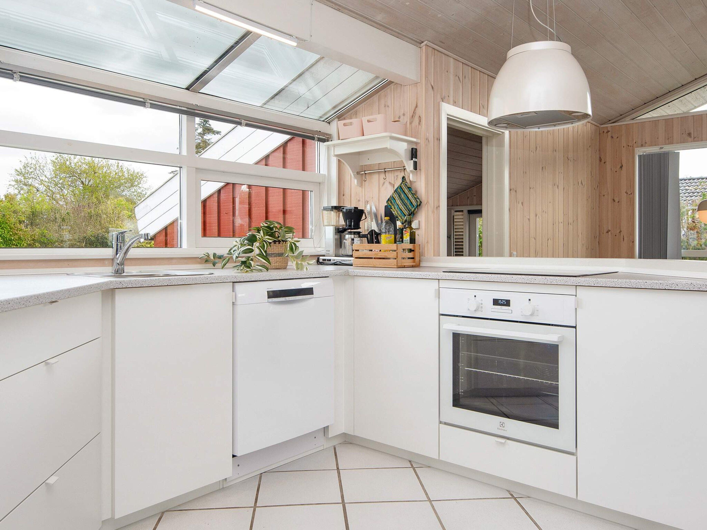 A modern kitchen with white cabinetry, a built-in oven, and a window overlooking a red building.