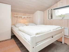 Habitación individual con una cama, techo de madera, ventana con persianas y una mesita de noche.