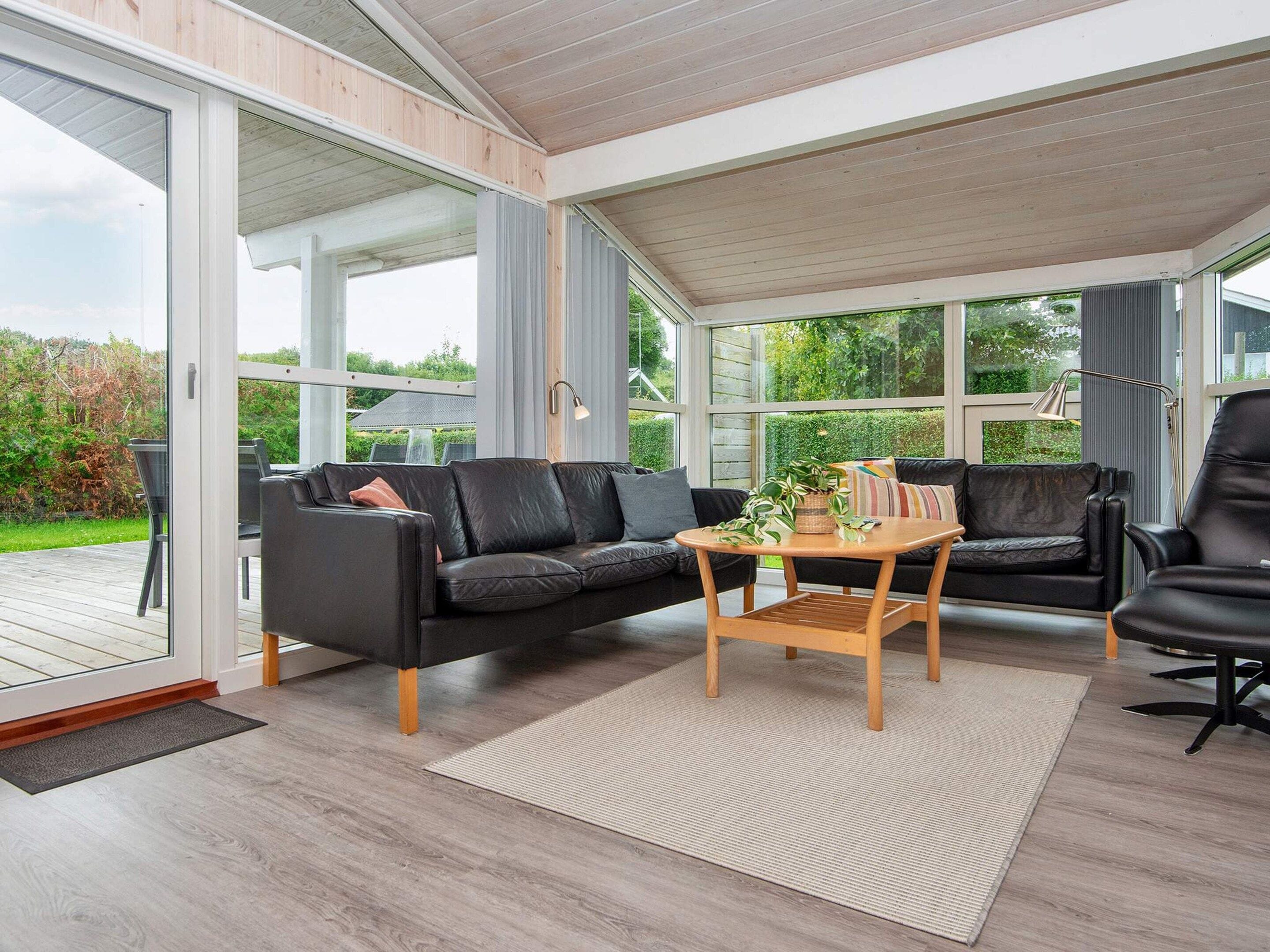 A sunroom with a black leather sofa, a wooden coffee table, and a view of the outdoors.