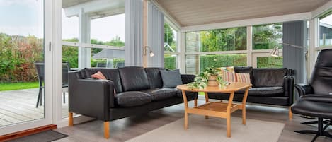 A sunroom with a black leather sofa, a wooden coffee table, and a view of the outdoors.