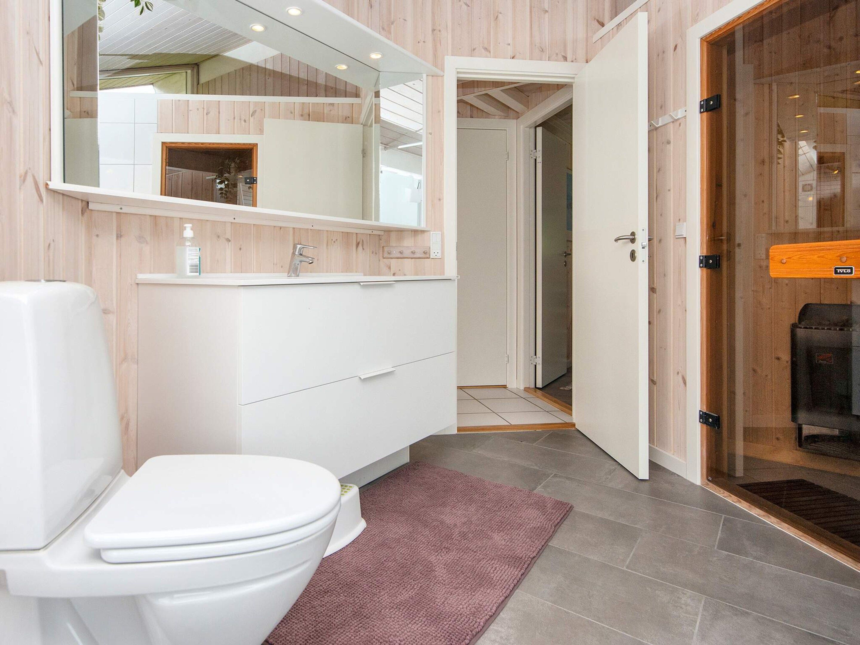 A bathroom with a white toilet, a sink with a mirror above it, and a wooden door leading to another room.