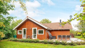 A wooden house with a tiled roof, a front door, and a small patio area with outdoor furniture. - 5 Star Holiday Home in Allingabro (Allingåbro)