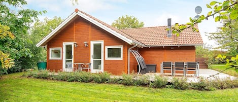 A wooden house with a tiled roof, a front door, and a small patio area with outdoor furniture.